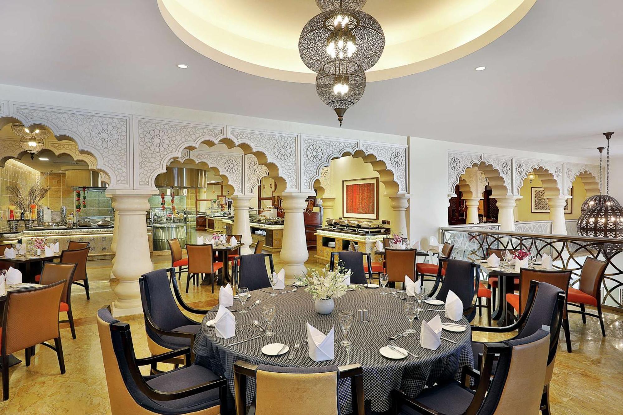 Hilton Suites Jabal Omar Makkah Mecca Exterior photo The photo shows an elegantly designed restaurant interior. The space features a round dining table set with plates, glasses, and folded napkins. Surrounding the table are modern, comfortable chairs. The walls are adorned with intricate architectural 