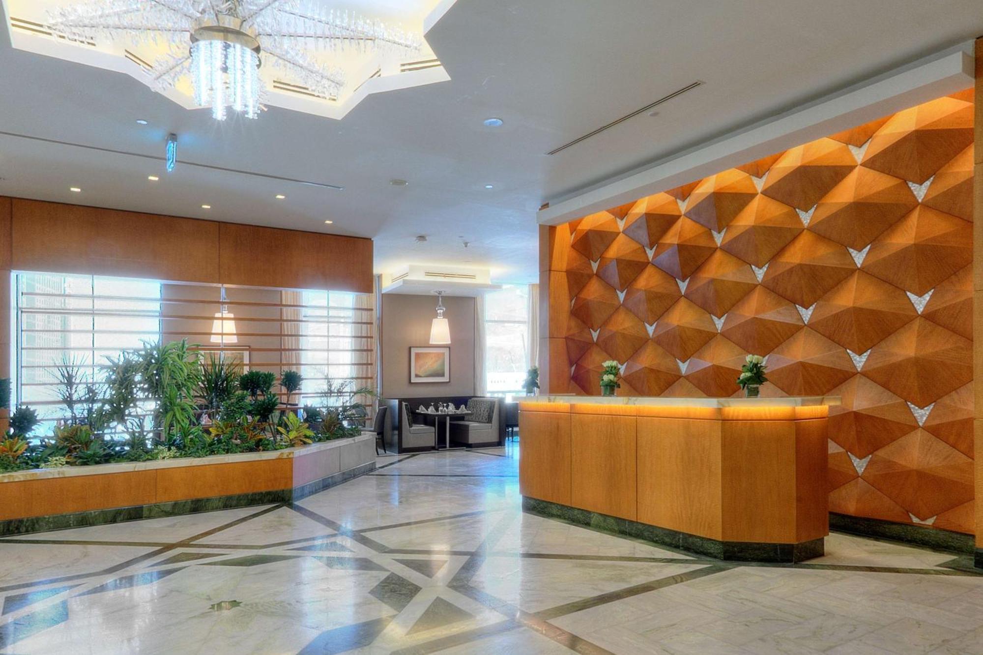 Hilton Suites Jabal Omar Makkah Mecca Exterior photo The photo shows a hotel lobby area. On the right side, there is a reception desk made of wood, featuring a modern design. Behind the desk, there is a decorative wall with a unique geometric pattern in shades of orange and brown. To the left, there ar