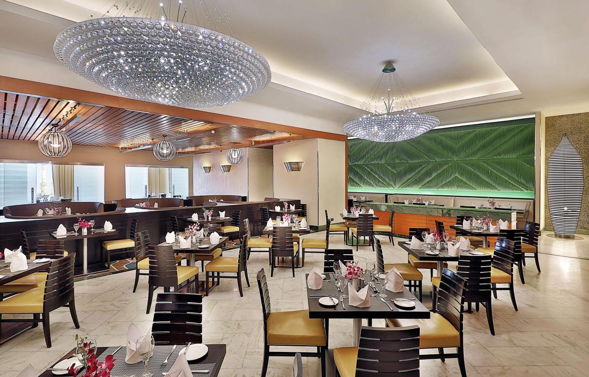 Hilton Suites Jabal Omar Makkah Mecca Exterior photo The photo features an elegant restaurant interior. It has a modern design with light-colored walls and wooden accents. The space is furnished with dark wooden tables and chairs, each set with neatly arranged tableware, including napkins and small cen