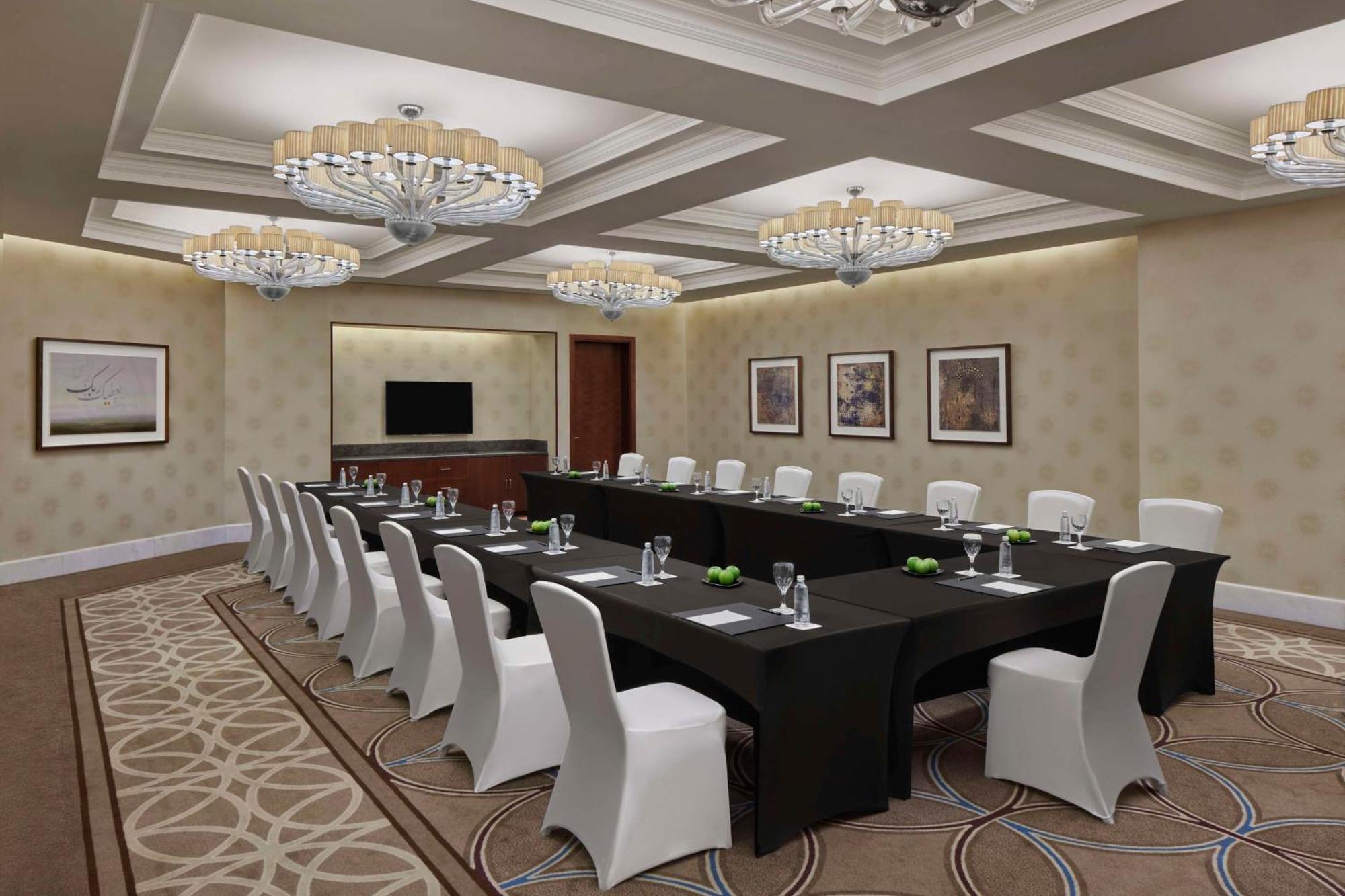 Hilton Suites Jabal Omar Makkah Mecca Exterior photo The photo shows a conference room set up for a meeting. There is a long table covered with a black tablecloth, surrounded by white chairs. The room is well-lit with elegant chandeliers hanging from the ceiling. The walls are painted in a light color,