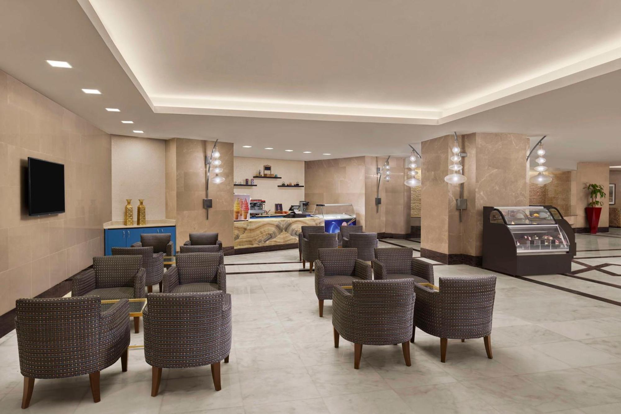 Hilton Suites Jabal Omar Makkah Mecca Exterior photo The photo depicts a modern and inviting lobby area, likely in a hotel or similar establishment. The space features a light-colored tiled floor and beige walls, creating a warm ambiance. 

In the foreground, there are several comfortable armchairs arr