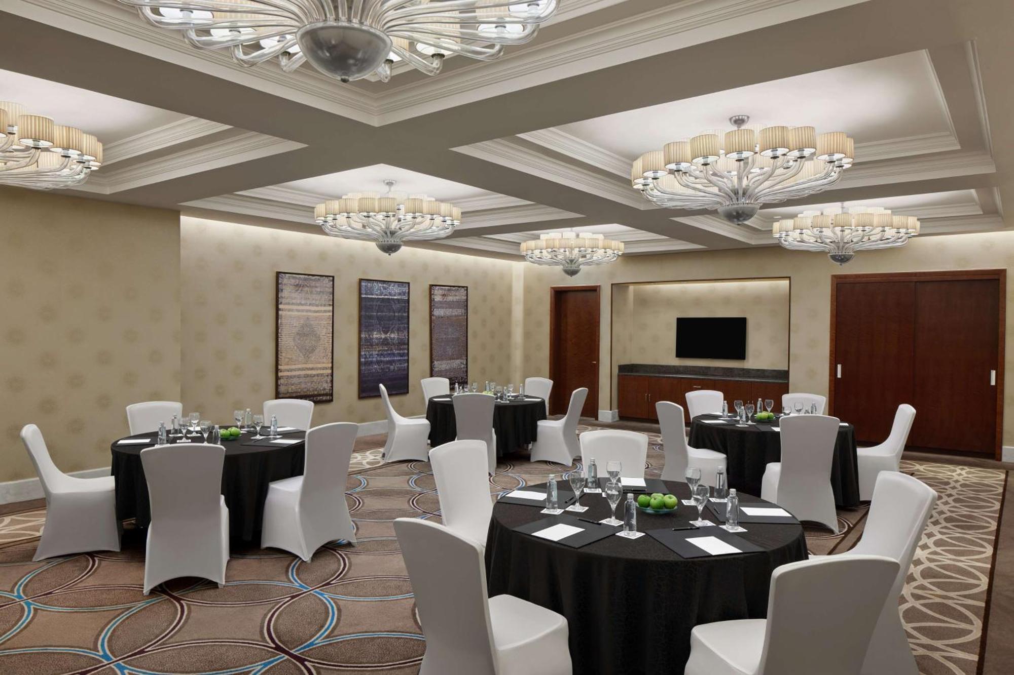 Hilton Suites Jabal Omar Makkah Mecca Exterior photo The photo shows an elegant banquet or conference room. It features several round tables covered with black tablecloths, each set with glassware, plates, and small green centerpieces. The chairs are white and neatly arranged around the tables. The roo