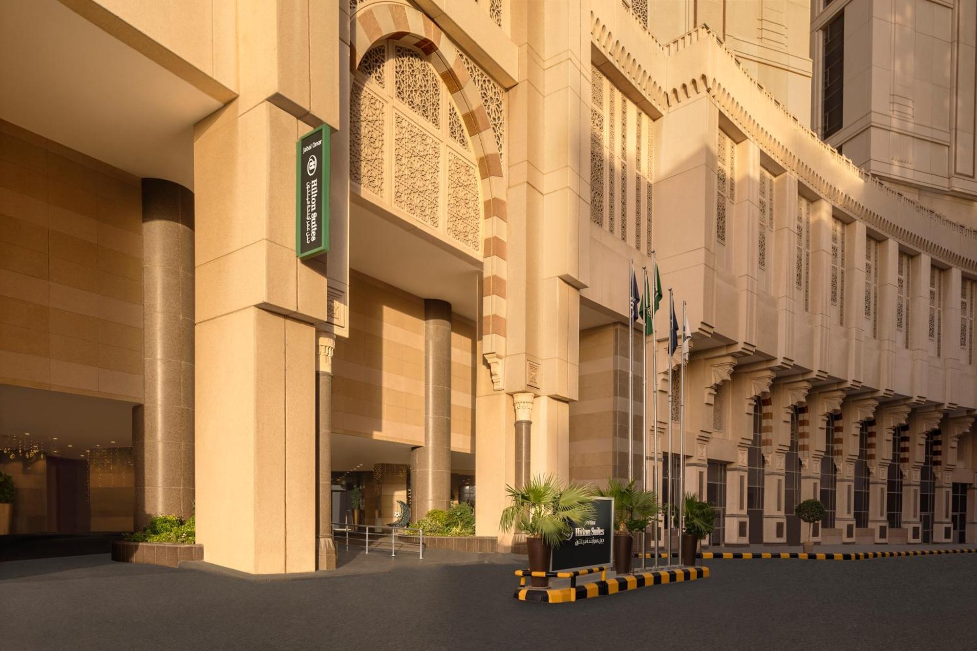 Hilton Suites Jabal Omar Makkah Mecca Exterior photo The photo shows a modern building with a distinctive architectural style, featuring large, light-colored stone facades. The entrance is prominent, with a wide, inviting pathway leading up to it. To the left, there is a sign that appears to indicate t