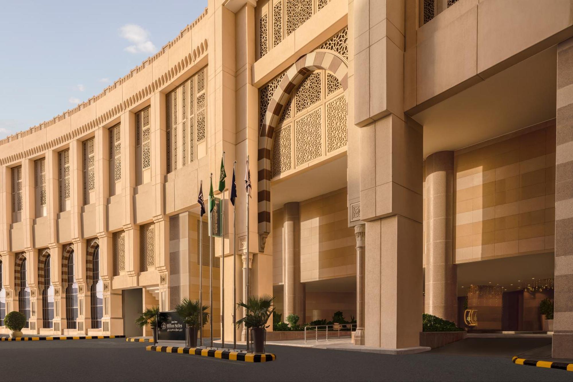 Hilton Suites Jabal Omar Makkah Mecca Exterior photo The photo shows a large, modern architectural structure with a grand entrance. The building features a curved facade and intricate design elements, suggesting a blend of contemporary and traditional architectural styles. Several flags are displayed i